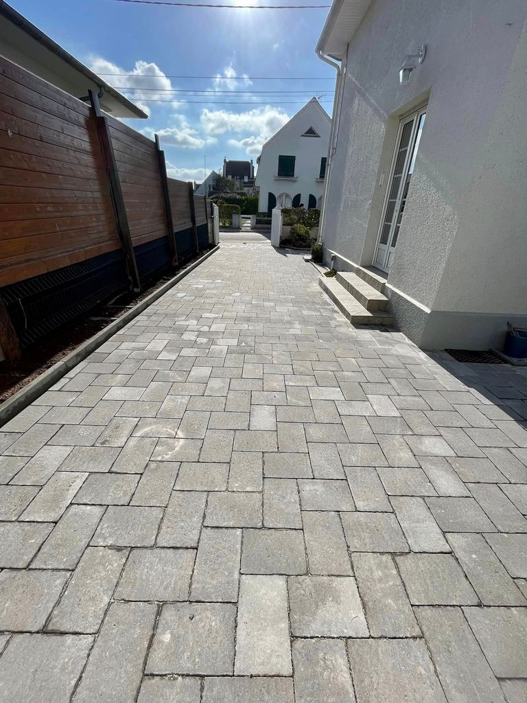Allée pavée entre une maison et une clôture bois