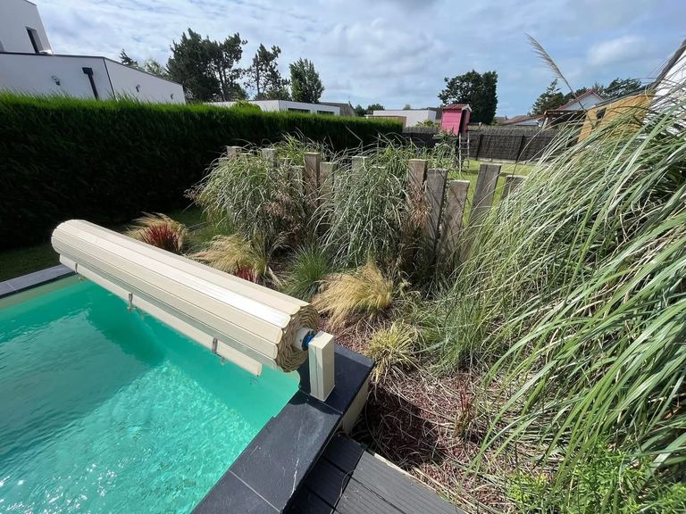 Bassin de piscine bordé d’un massif de graminées et de poteaux bois